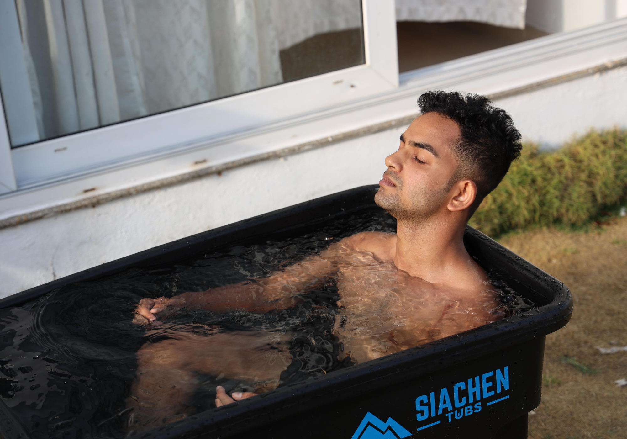 Man flexing muscles in front of a black ice bath tub