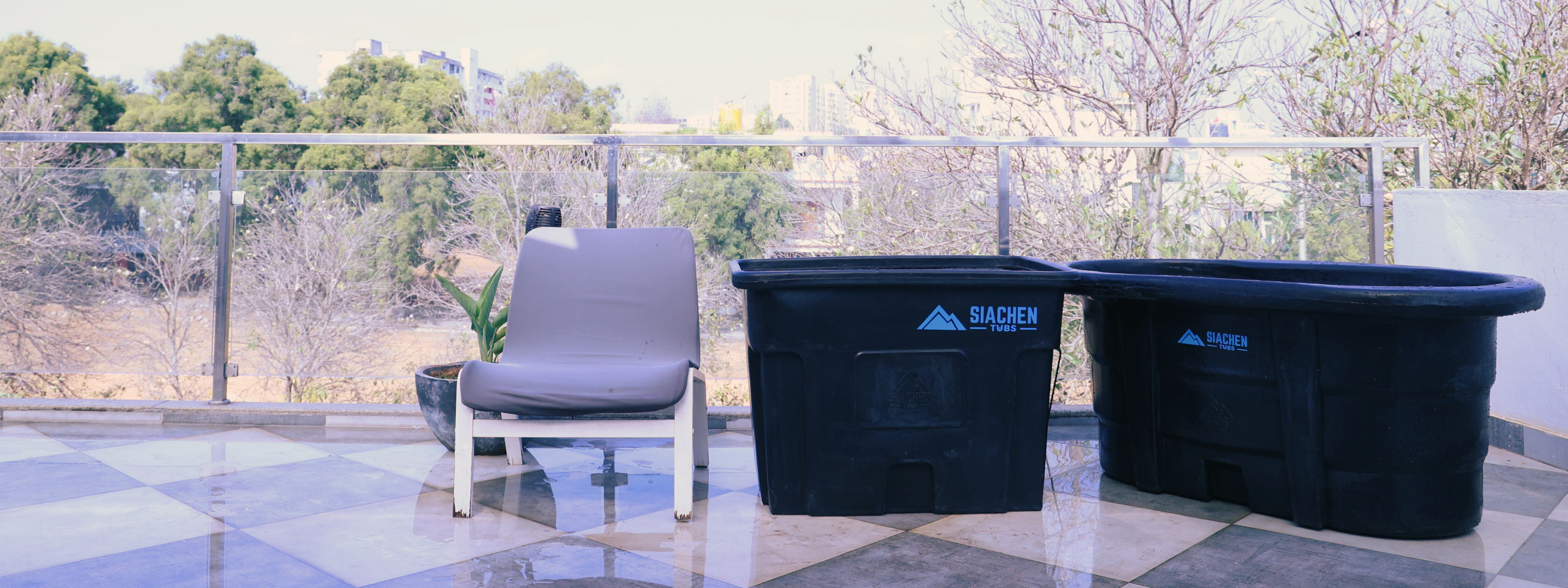 Two black plastic storage ice bath tubs on a patio with a chair and plants in the background. 